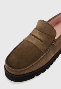 Loafers din suede maro cu o textură netedă, având o bandă proeminentă și detalii cusute. Talpă din cauciuc negru cu un finisaj texturat.