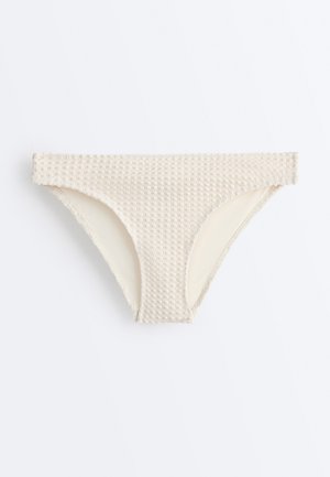 Beige bikinibroekje met textuur en een hoog uitgesneden pijp, platliggend op een witte achtergrond.