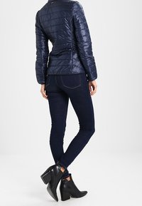 Mörkblå puffjacka med horisontella sömmar, kombinerad med mörka skinny jeans och svarta ankelboots med klack och dragkedjedetalj.