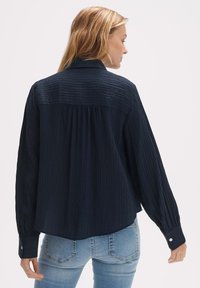 Navy long-sleeve shirt with vertical ribbed texture. Button cuffs and pleated back detail, featuring a rounded hem. Casual fit.