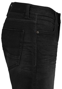 Black denim jeans with a fitted shape, featuring traditional pockets, stitching details, and a back leather patch. Textured fabric.