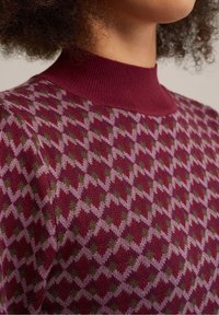 Bourgogne stickad tröja med hög ribbad halsrinning, prydd med ett geometriskt diamantmönster i nyanser av rosa och grönt, mjuk textur.