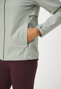 Lichtgroene windbreaker met een ritszak aan de zijkant en verstelbare manchetten. Beschikt over een zachte textuur en een minimalistisch ontwerp.