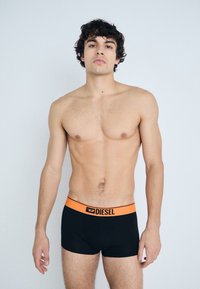 Caleçons boxers noirs avec une taille en logo orange de Diesel. Le tissu paraît lisse, et le design est ajusté avec une forme simple.