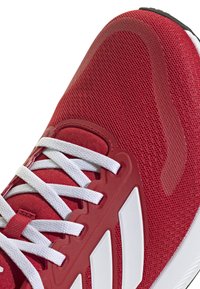 Red athletic shoe featuring a breathable mesh upper, white laces, and three white stripes on the side. Textured rubber sole.