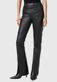 Black leather trousers with a fitted design, straight legs, and side slits at the hem. Smooth texture with a glossy finish.