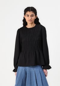 Black long-sleeve top featuring gathered texture, a round neckline, and a fitted bodice with a flared hem. Paired with a light blue pleated skirt.