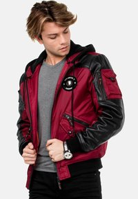 Rote und schwarze Bomberjacke aus Nylon, mit Kapuze, Reißverschlusstaschen und einem Logo-Patch auf der Brust. Texturierte, lederähnliche Ärmel.
