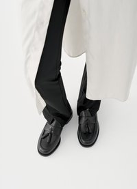 Μαύρα δερμάτινα μοκασίνια με φούντες, λεία υφή και στρογγυλεμένη μύτη, συνδυασμένα με μαύρο παντελόνι και φωτεινό πουκάμισο σε πιο φαρδιά γραμμή.