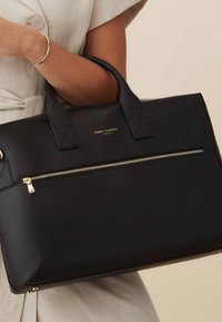 Sac à main en cuir noir avec double poignée, design structuré, poche zippée à l'avant, quincaillerie dorée et détails du logo. Fini texturé.
