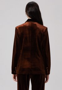 Blazer en velours marron présentant un design ajusté, un col cranté et des détails de bouton aux manches. Texture lisse et couleur unie.