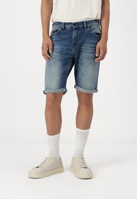 Hellblaue Denim-Shorts mit umgeschlagenem Saum, ausgestattet mit zwei vorderen Taschen und einer hinteren Tasche, getragen mit weißen Socken und beigen Sneakers.