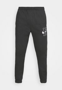 Svarta träningsbyxor med elastisk midja och muddar, prydda med en vit logotyp på sidan, tillverkade av mjukt material med en slät yta.