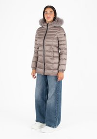 Giubbotto imbottito in taupe tenue con colletto in ecopelliccia, motivo a righe verticali, chiusura con zip e polsini elastici; abbinato a jeans a gamba larga blu.