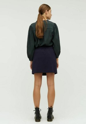 Grønstribet langærmet blouse med pufærmer, parret med en navy mini-nederdel og sorte ankelstøvler med snøredetaljer.