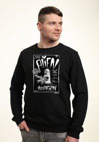 Felpa nera con un design grafico che raffigura un alieno e la scritta "ALIEN INVASION". Il tessuto sembra morbido con una vestibilità comoda.