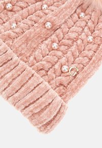 Šviesiai rožinė megzta kepurė, pagaminta iš pūkuotos medžiagos, su kabelių mezgimo raštu, dekoratyvinėmis dirbtinėmis perlų detalėmis ir mažo aukso logotipo akcentu.