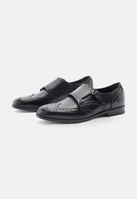 Scarpe in pelle nera con dettagli brogue, dotate di doppia fascia e chiusura con fibbia. Punta tonda e suola piatta, texture liscia.