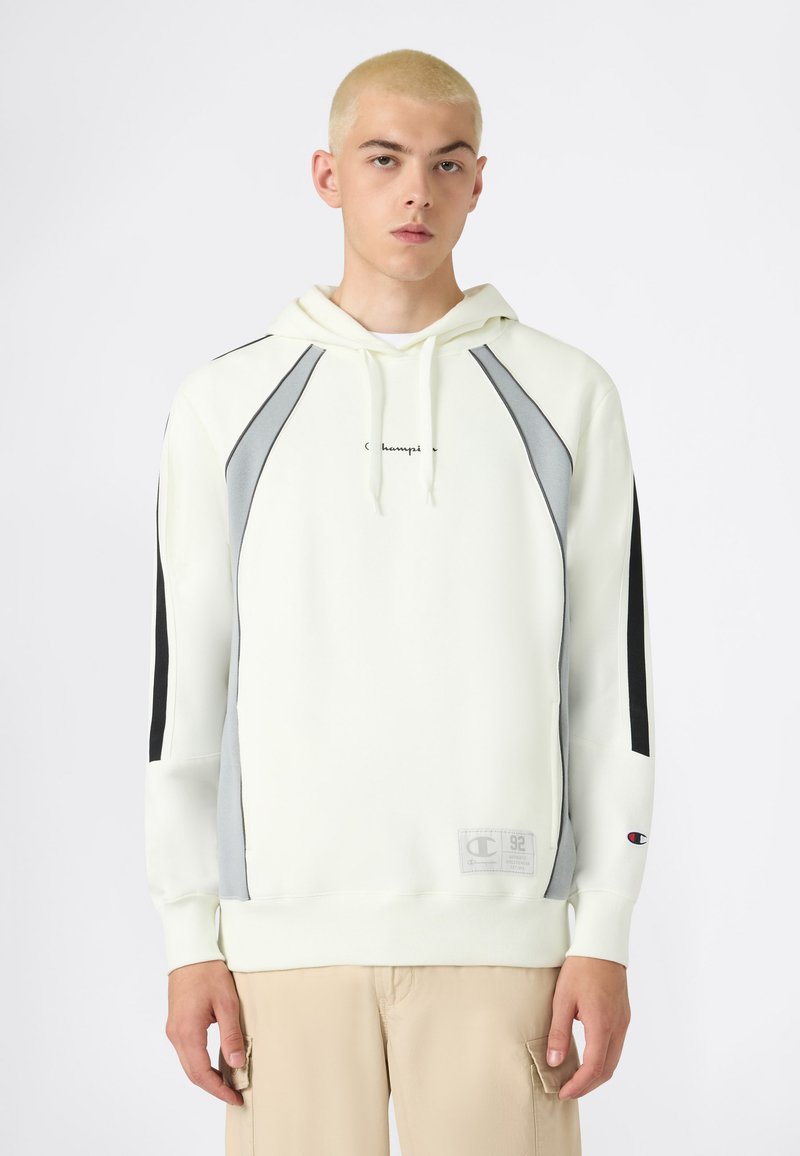 Felpa leggera colore crema con accenti grigi e neri, dotata di tasca a marsupio, cappuccio con cordino e patch con logo sull'orlo. Tessuto dalla consistenza liscia.