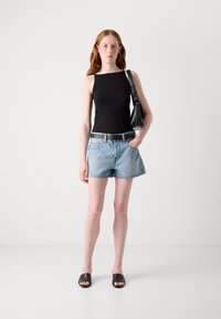 Svart ermeløs topp, lys blå mønstret denimshorts, svart belte og svarte sandaletter. Modellen holder en liten svart håndveske.