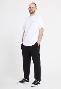 Biała bawełniana koszulka z małym logo, w połączeniu z czarnymi spodniami dresowymi z logo na lewym kieszeni. Obuwie to czarne trampki.