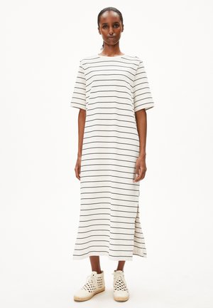Robe midi rayée en blanc avec des rayures horizontales noires, dotée de manches courtes, d'un col rond et d'entailles sur les côtés. Portée avec des chaussures en osier.