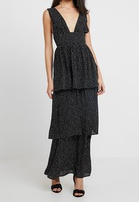 Robe noire avec un décolleté en V profond, taille froncée et design en couches. Présente de petits pois blancs et une texture de tissu fluide.