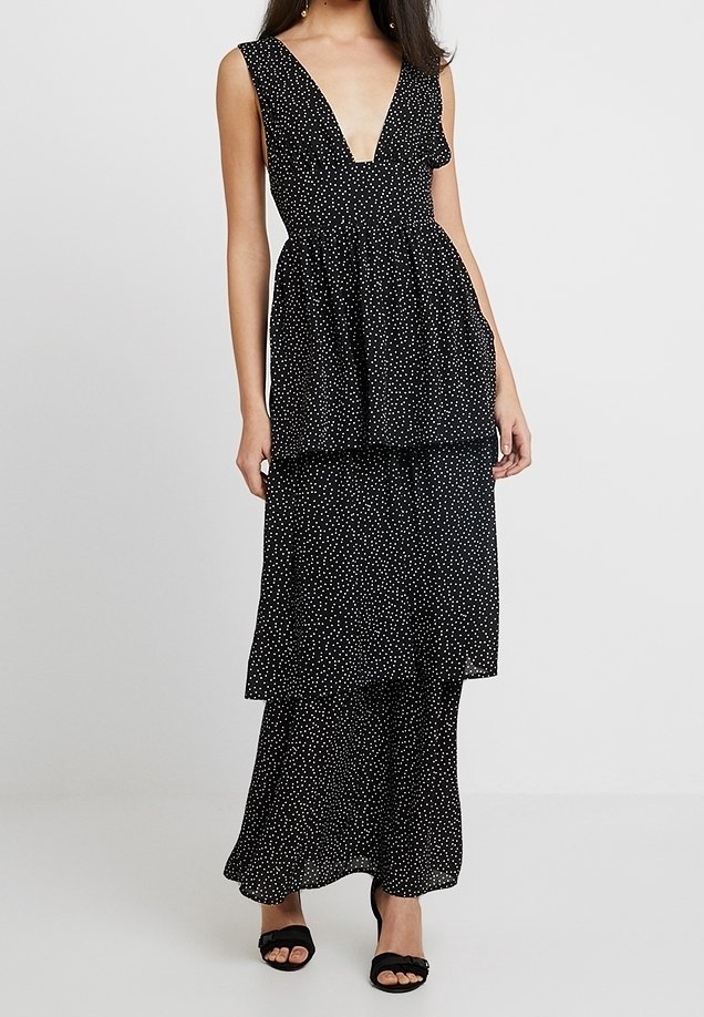 Robe noire avec un décolleté en V profond, taille froncée et design en couches. Présente de petits pois blancs et une texture de tissu fluide.