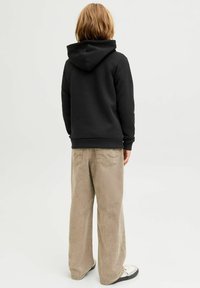 Felpa nera con cappuccio ampio, abbinata a pantaloni larghi color beige chiaro. Il tessuto sembra morbido, con cuciture visibili e tasche.