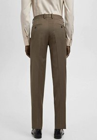 Braune, maßgeschneiderte Hose mit geradem Bein, Gürtelschlaufen und zwei Gesäßtaschen, kombiniert mit einem hellen, geknöpften Hemd.