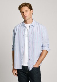 Light blue button-up shirt with vertical red and white stripes, chest pocket, relaxed collar, worn over a white graphic t-shirt.