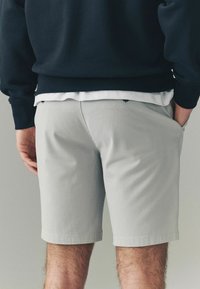 Pantalones cortos de color gris claro hechos de tela tejida, con un corte recto, bolsillos laterales y un dobladillo limpio. Llevados con un suéter azul marino encima.