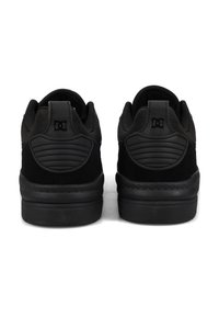 Černé tenisky s texturovaným svrškem a hladkým panelem, který má polstrovaný límec a akcent s logem na patě. Plochá gumová podrážka.