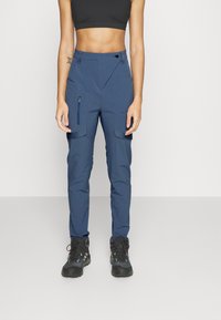 Marina blå cargobyxor med smal passform, tillverkade av lätt material, med zippered fickor och tryckknappsstängning. Mörka skor.