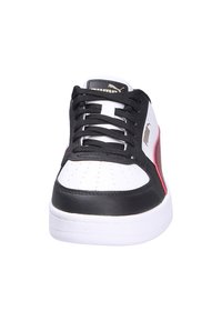 Zapatilla baja de Puma con base blanca, superposiciones negras, franja lateral roja, cordones negros y suela blanca, vista desde el frente.