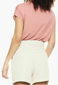 Růžová košile s krátkým rukávem a ohrnutými manžetami zkombinovaná s bílými šortkami s vysokým pasem, které mají texturovaný vzor a dvě zadní kapsy.