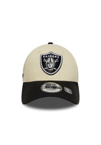 Boné ajustável bege com aba preta, apresentando um proeminente logotipo dos Raiders em preto e prateado na parte da frente. Material de poliéster texturizado.