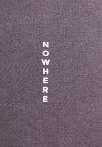 Tessuto grigio con testo verticale bianco che recita "NOWHERE." Texture morbida con un design semplice e moderno. Nessun motivo o accento aggiuntivo.