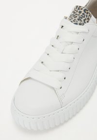 Weiße Ledersneaker mit flachen Schnürsenkeln und einer strukturierten Gummisohle. Mit einem Leopardenmuster-Akzent an der Ferse. Glatte Oberfläche, runde Zehenpartie.