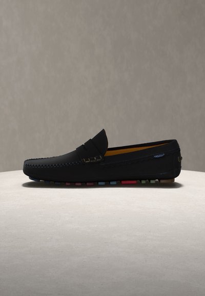 Μαύρο δερμάτινο μοκασίνι με λουράκι penny, εμφανή ραφή και λεπτομέρειες πολύχρωμης λαστιχένιας σόλας σε ανοιχτό φόντο.