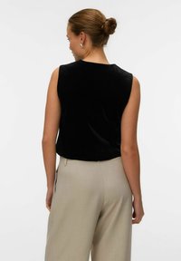 Top senza maniche in velluto nero, design aderente, lunghezza corta, abbinato a pantaloni a gamba larga beige chiaro, texture liscia, minimalismo nei dettagli.
