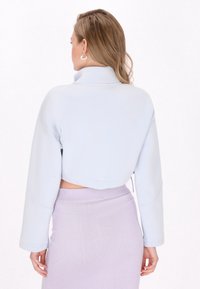 Jasnoniebieska krótka kurtka z miękkiego materiału, z długimi rękawami i wysokim kołnierzem, w połączeniu z prążkowaną, liliową spódnicą.