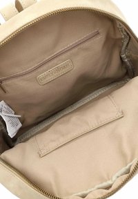 Interno di uno zaino beige con una tasca con cerniera e un'etichetta in tessuto. Texture liscia e bordi rifiniti, con un motivo discreto nella fodera.