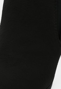 Gros plan sur une surface de tissu noir texturé avec des coutures visibles le long du bord.