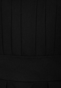 Gros plan d'un tissu noir avec des plis verticaux et une large bande horizontale autour de la taille.