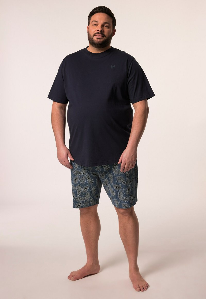Camiseta de algodón azul marino de manga corta combinada con pantalones cortos estampados que presentan motivos de hojas en verde y beige, usados descalzo.