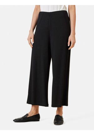 Zwarte wijde broek gemaakt van zachte stof, met een elastische tailleband en een soepele, vloeiende uitstraling. Gecombineerd met zwarte instappers.