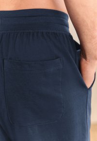 Navy blue lounge shorts with an elastic waistband and a single back pocket. The fabric appears soft and smooth, with subtle texture.