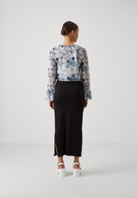Blus med blommönster, genomskinlig och med långa ärmar i blått och vitt, i kombination med en figursydd svart kjol med en sidoklyfta, kompletterad av vita klackar.
