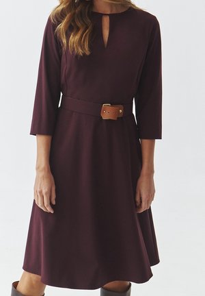 Mørkerød midi kjole med trekvartærmer, nøglehul-udskæring og et brunt bælte med en guldfarvet spænde. Glat stof med en flagrende skørt.